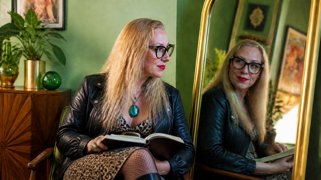 Sherry Martin seated beside a vintage mirror with her journal in a colorful mid-century-modern home